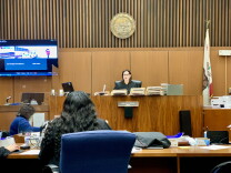 The inside of an L.A. courtroom. A female judge who appears to be white sits at the bench. To her left, a large screen shows images related to the case; they are difficult to make out. 