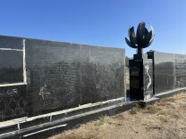 A diagonal view of a black granite wall with the outline of names vaguely visible on the surface and an internal flame in the center with a map of Vietnam engraved on it. 