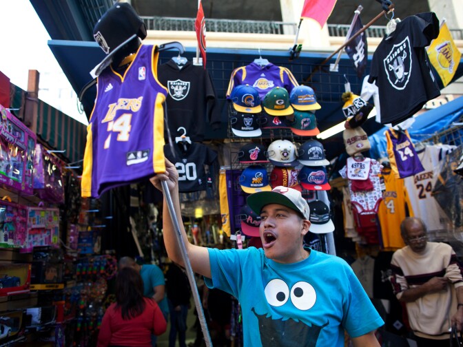 Jose Gonzalez advertises his sports merchandise store in Santee Alley as shoppers buy last-minute gifts on Christmas Eve.