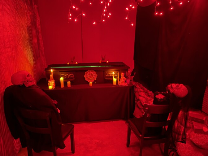 A room lit in blood red with an altar and two skeletons sitting in chairs
