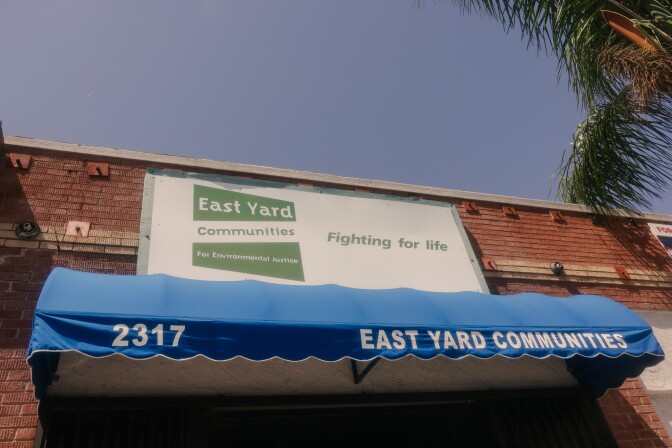 The front of a building shown with a blue sky and part of a palm tree above it. 