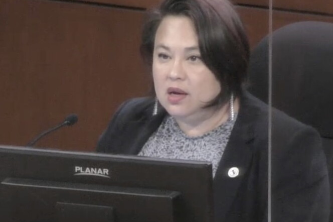A Korean American woman of 50 with a bob sits at the city council dais.