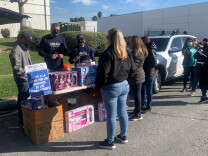People stand outside of Jon Donaire's building for a toy drive. There are toys on a table, and a sign that reads "Unete a la lucha por los derechos de los trabajadores."