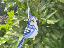 A hand crafted ceramic ornament depicting a blue jay hangs in a tree. 