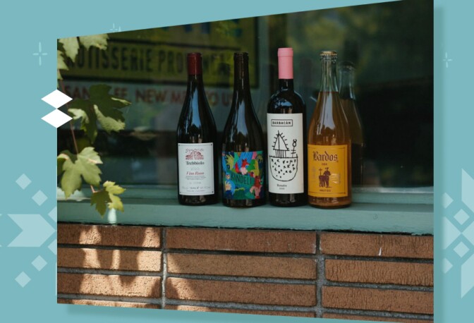 A group of four wine bottles sits on a brick wall in front of a window.