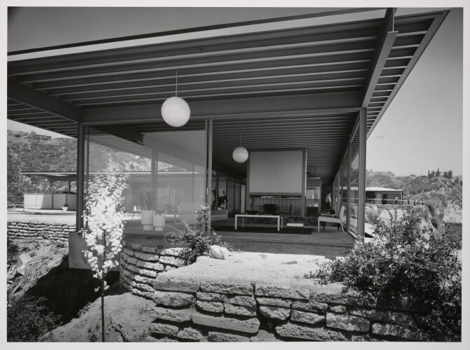 A black and white photo of a mid-century modern home taken from the outside looking into the living room. 