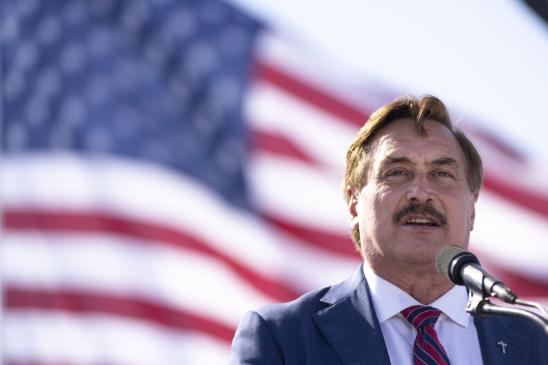 Mike Lindell stands at a mic in front of a U.S. flag.
