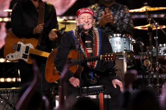  Willie Nelson sitting on stage with his guitar. 