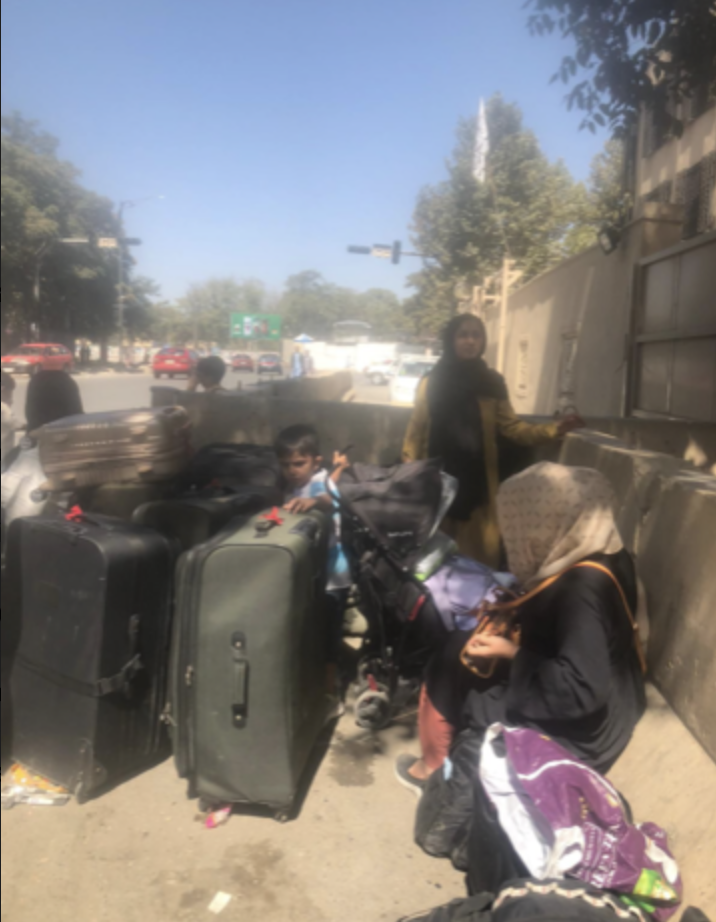 A family camps outside the Kabul airport with suitcases, just off a public street with cars driving by.