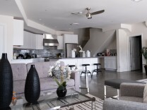 A grey and white living room and kitchen with black accented furniture and decorations.