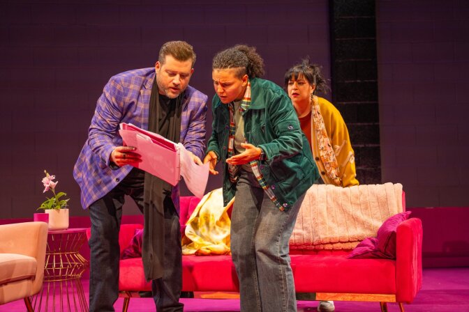 Stage production with three actors, two of whom are reading something. 