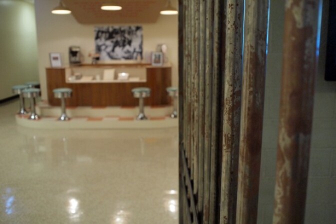 A detail of the Clayton Museum and Library's "Get On Board" Exhibition. In the foreground, a reproduction of the jail cell freedom riders were confined to after attempting to eat at a Houston lunch counter. In the background, a reproduction of the counter.