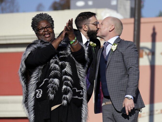Aubrey Loots, right, and Danny Leclair, the first gay couple to be married aboard a float in the Tournament of Roses, kiss after being wed by the Rev. Alfreda Lanoix of the Unity Fellowship Church of Christ, left, aboard the AIDS Healthcare Foundation float in the 125th Rose Parade in Pasadena, Calif., Wednesday, Jan. 1, 2014. (AP Photo/Reed Saxon)