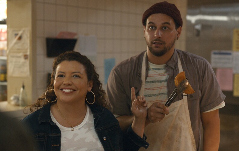 Photo of two people, one of them is holding a empanada with tongs.