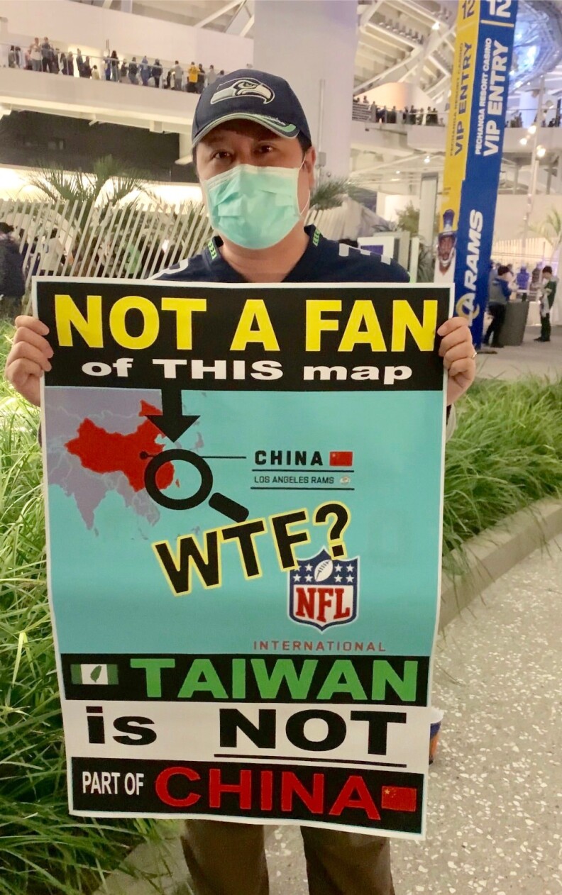 A masked Asian American man holds a printed sign that reads "Not a Fan of this map' and "Taiwan is not China."