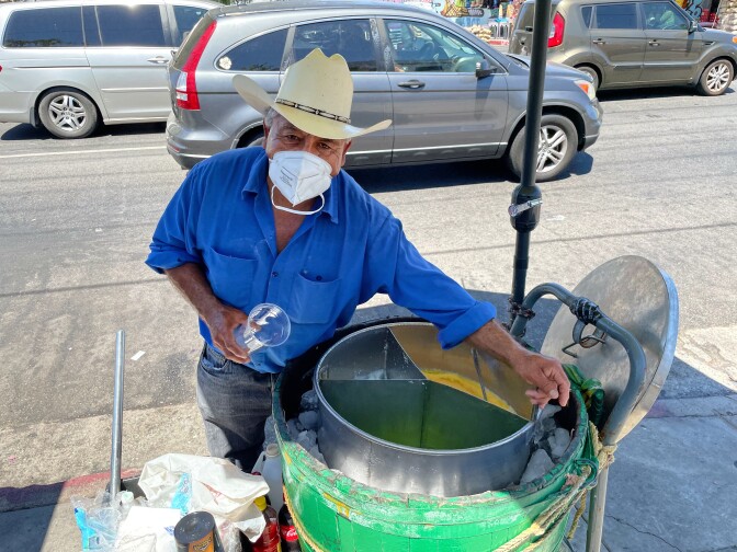 a man in a cowboy hat and face mask attends to a large metal vat containing ice cream