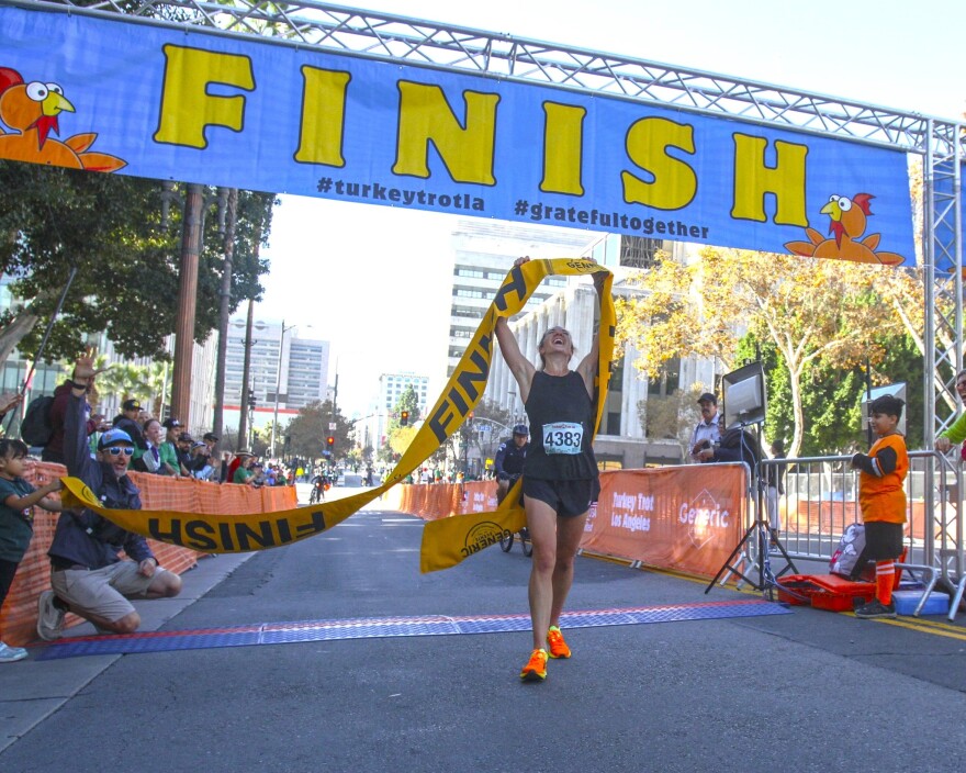 A runner holds the finish line ribbon abover their head as they complete a turkey trot race.