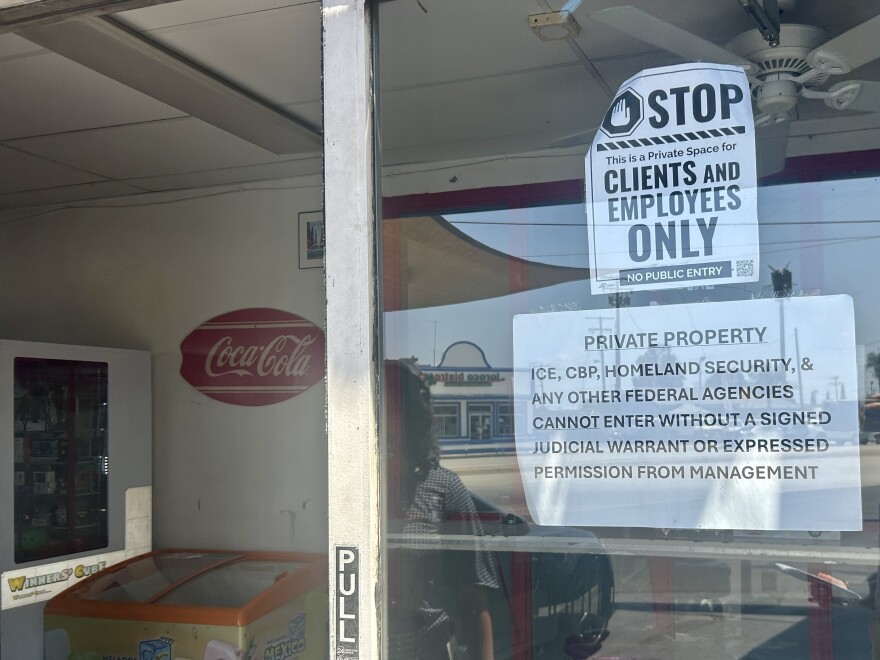 The waiting room of a car wash. A glass door fills the right side of the image, which says 'pull' near the handle. On the glass facing us are two printed 'private property' signs on top of one another. The one on top reads 'STOP: This is a private space for clients and employees only.' The one on the bottom reads 'Private property: ICE, CPB, Homeland Security, & any other federal agencies cannot enter without a signed judicial warrant or expressed permission from management.