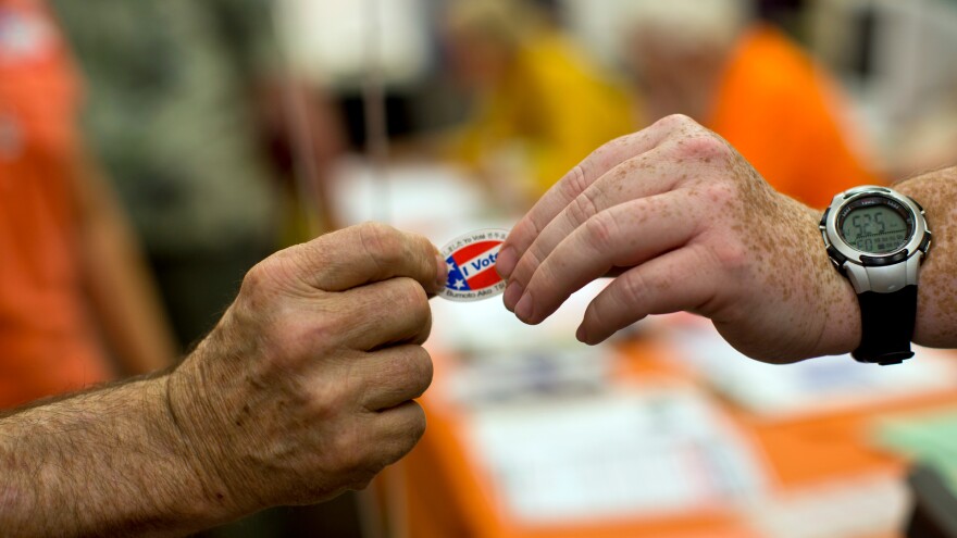 FILE: Poll clerk Patrick Meacham, right, hands a sticker to a voter at Canyon Springs School's library on Tuesday evening, June 3 in Santa Clarita.