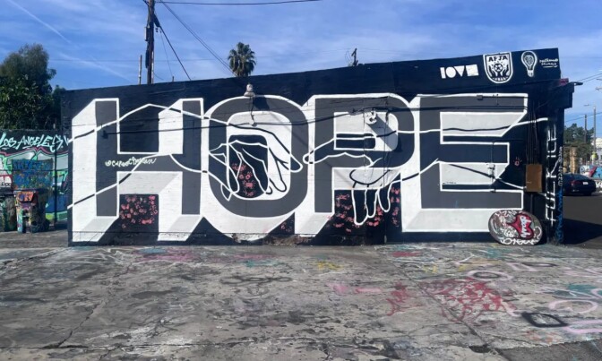 A small building with a mural that says "hope" in large letters and two hands reaching out for each other