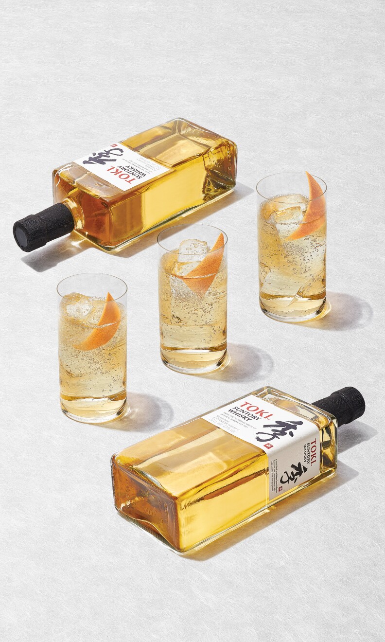 Three shot glasses filled with a cocktai centered between bottles of Toki Suntory whiskey.