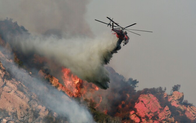 MALIBU, CA - NOVEMBER 11: A helicopter drops flame retardant on a wildfire on November 10, 2018 in Malibu, California. The Woolsey fire has burned over 70,000 acres and has reached the Pacific Coast at Malibu as it continues grow.  (Photo by Sandy Huffaker/Getty Images)