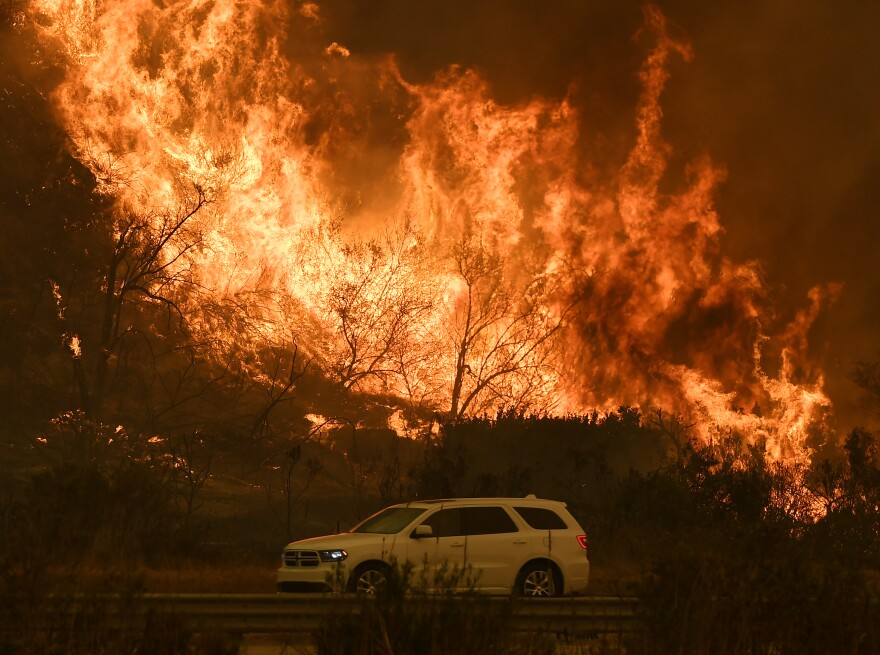 Vehicles pass beside a wall of flames on the 101 highway as it reaches the coast during the Thomas wildfire near Ventura, California on December 6, 2017. California motorists commuted past a blazing inferno Wednesday as wind-whipped wildfires raged across the Los Angeles region, with flames triggering the closure of a major freeway and mandatory evacuations in an area dotted with mansions. / AFP PHOTO / MARK RALSTON (Photo credit should read MARK RALSTON/AFP/Getty Images)