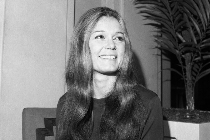 Black and white photo of a woman. She is seated, looking off to her left, smiling.