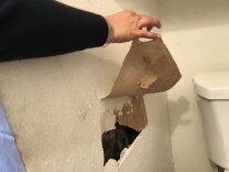 A woman points out for a large hole in the walls of her apartment.