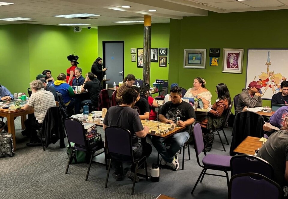 A room with green walls with people sitting at tables and playing games.