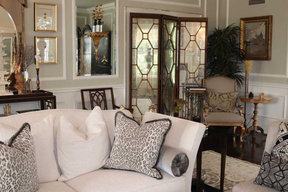 A formal living room with a white couch that has both white and leopard-skin patterned pillows. There are gold accents and mirrors throughout the room. 