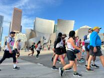 Runners and walkers running past a silver building in odd shape