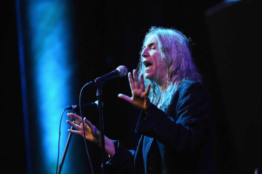 Patti Smith, bathed in a spotlight, sings at a mic on a dark stage at the Anthology Film Archives Benefit And Auction in 2017.