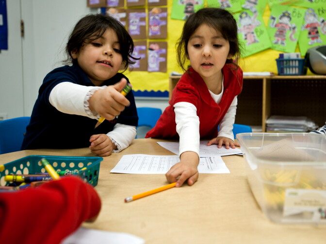 Transitional kindergarten students Adamaris Duran, left, and Sophia Lopez reach for pencils to begin a writing exercise.