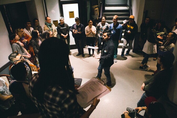 A couple dozen people stand in a circle inside a building lobby. 