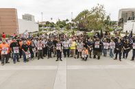 A group of people holding union signs and flags stands in front of a government building. 