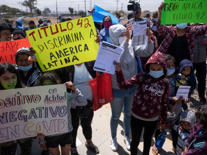 Protesters carry handwritten signs. One reads: "Titulo 42 Discrimina A America Latina"