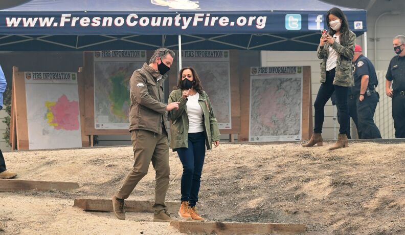A man and woman in black masks speak in front of a pop-up tent with large maps of the fire zone.