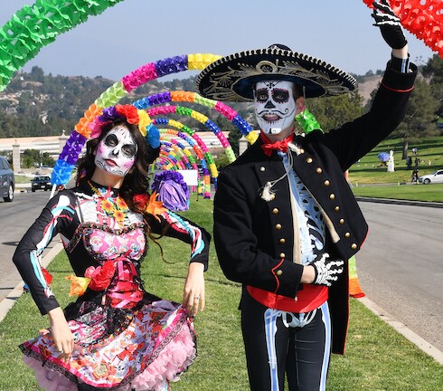 A Catrina and a Mariachi pose under a tunnel of rainbows at Forest Lawn’s Day of the Dead event