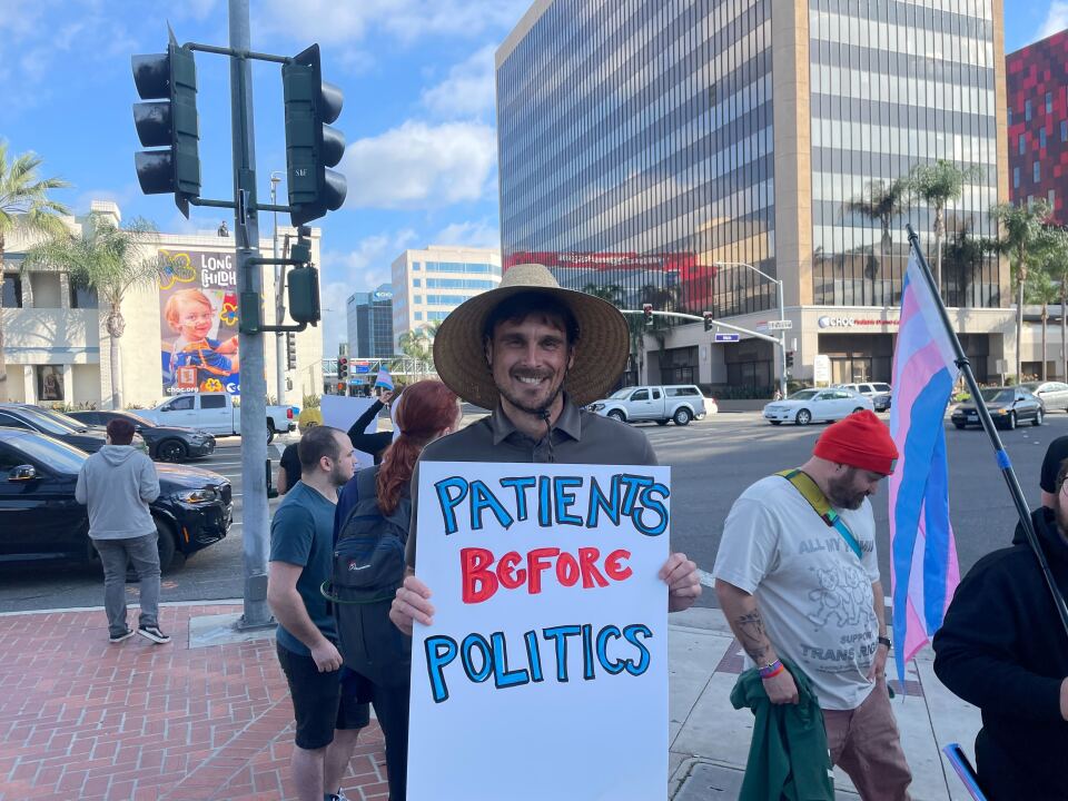 A man poses at a rally with a sign that says "patients before politics."