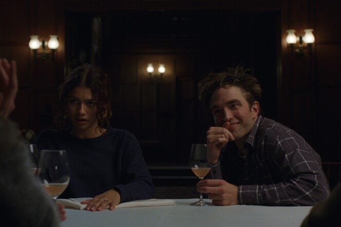 A female presenting person and a male presenting person sitting side by side at a table, across from two other figures who are not visible. Wine glasses are on the table.
