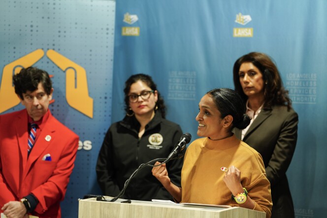 A woman speaks at a podium as three people look on from behind.