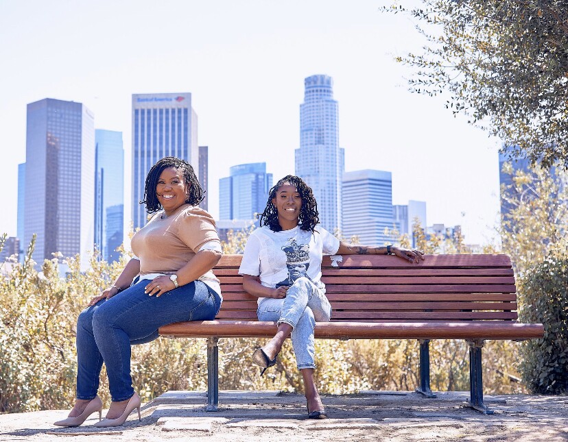 Evette Ellis and Kameale C. Terry, co-founders of ChargerHelp!, pose on a bench overlooking downtown Los Angeles. 