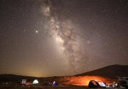 Bright objects in the night sky appear in a very starry sky over a campsite. 