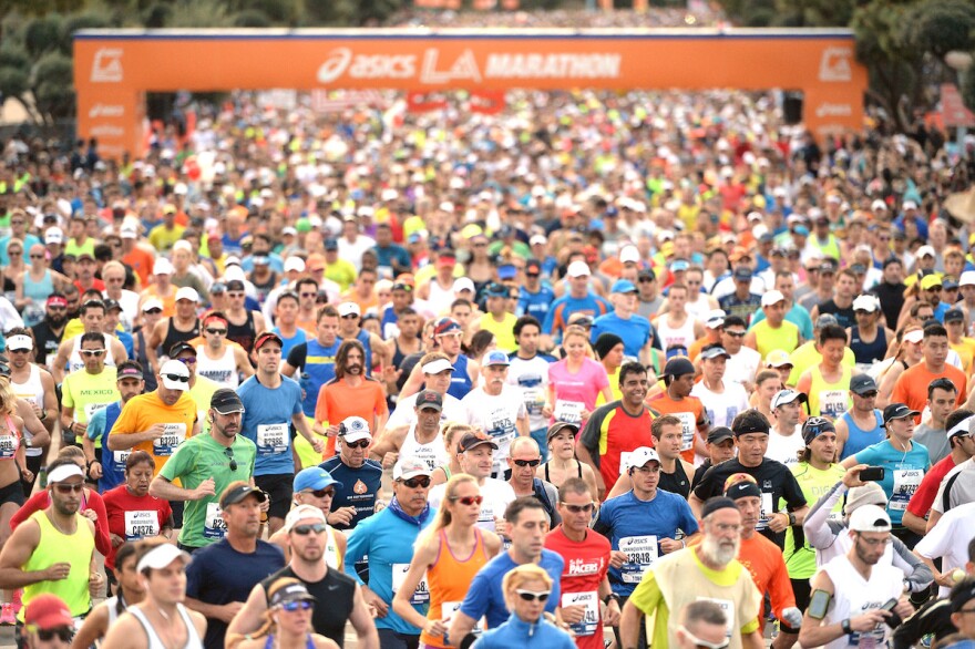 A picture of a Los Angeles marathon that has just started. Thousands of people wearing numbers pinned to their chests run.
