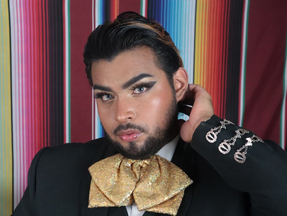An image of Ayan Vasquez Lopez, who is wearing a gold tie with a mariachi suit and his signature makeup look with a winged eyeliner tip.