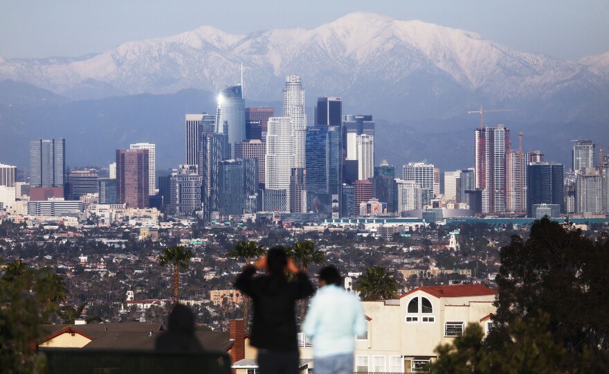 LOS ANGELES, CALIFORNIA - FEBRUARY 11:  A man takes photos with snow-capped mountains standing behind the skyline of downtown of the city on February 11, 2019 in Los Angeles, California. A series of snowstorms and rainstorms in California in recent weeks have drastically reduced drought conditions across the state, with only ten percent of the state now considered in conditions of moderate or extreme drought. (Photo by Mario Tama/Getty Images)