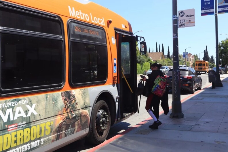 A woman carrying a multicolor backpack enters an orange public transit bus.