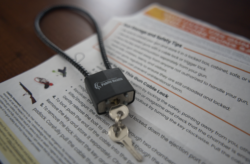A looped steel cable joined with a lock with protruding keys sits on a flyer explaining how to use a gun lock.