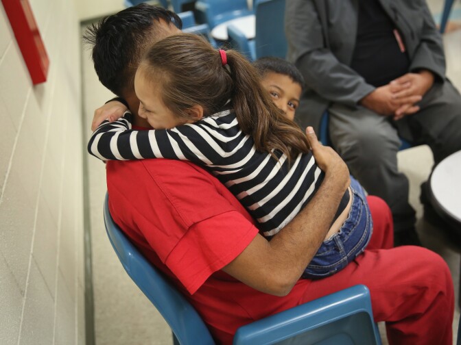 ADELANTO, CA - NOVEMBER 15: An immigrant detainee holds his children during a family visitation visit at the Adelanto Detention Facility on November 15, 2013 in Adelanto, California. The facility, the largest and newest Immigration and Customs Enforcement (ICE), detention center in California, houses an average of 1,100 immigrants in custody pending a decision in their immigration cases or awaiting deportation. The average stay for a detainee is 29 days. The facility is managed by the private GEO Group. ICE detains an average of 33,000 undocumented immigrants in more than 400 facilities nationwide. (Photo by John Moore/Getty Images)